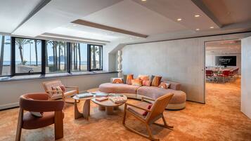 A modern living room with a large window, a sectional sofa, a coffee table, and a dining area visible through an open door.