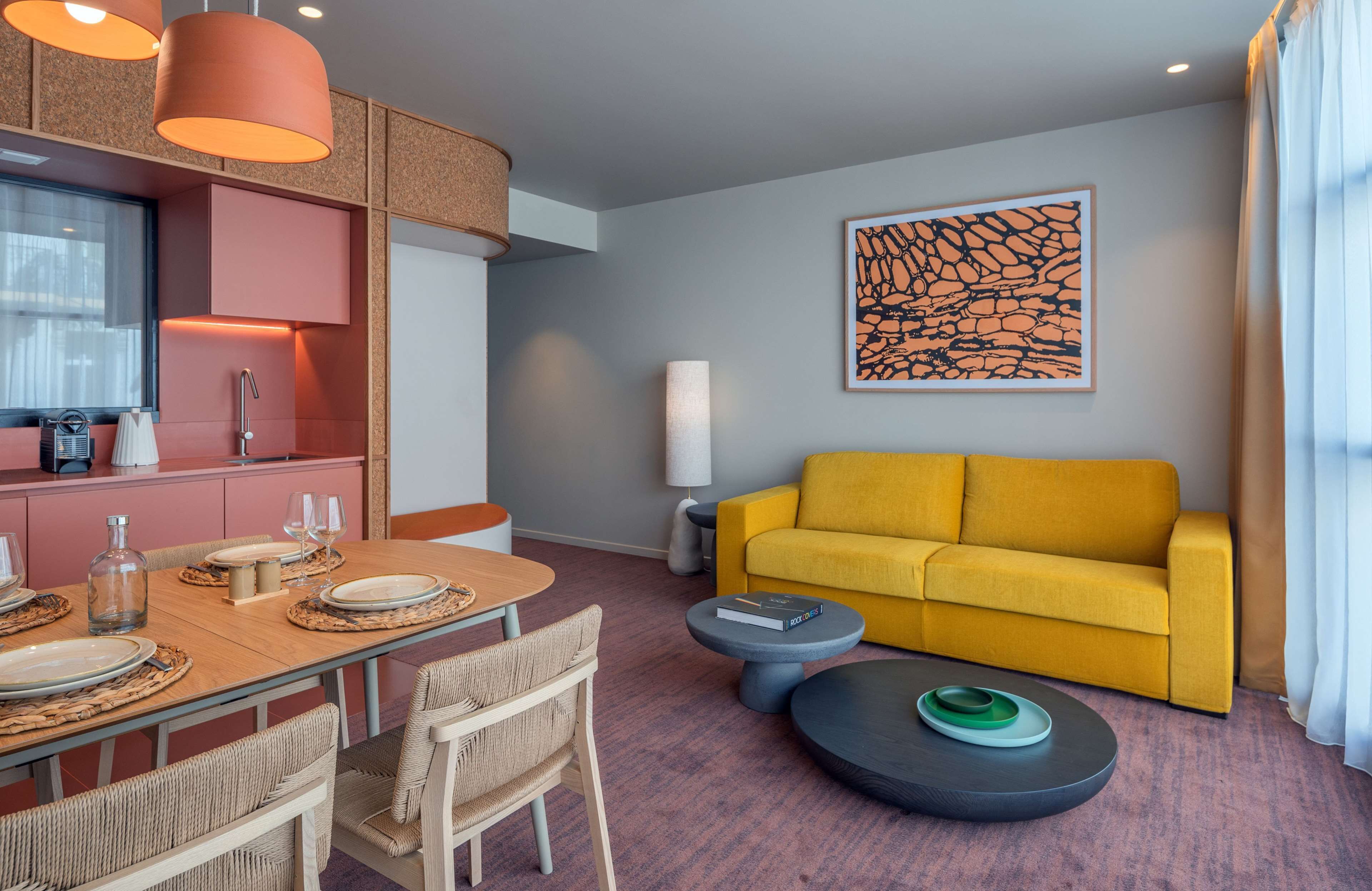 Un soggiorno moderno con un divano giallo, un tavolo da pranzo apparecchiato con piatti e bicchieri, un tavolino da caffè e un grande quadro astratto appeso al muro.