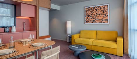 Una sala moderna con un sofá amarillo, una mesa de comedor dispuesta con platos y vasos, una mesa de centro y un cuadro abstracto grande en la pared.