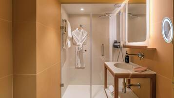 Une salle de bain moderne avec une douche à parois de verre, un meuble-lavabo en bois et un miroir doté d’un cadre éclairé.
