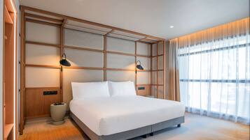 Un dormitorio moderno con una cama grande, cabecera de madera, lámparas de noche y vistas al exterior a través de cortinas translúcidas.