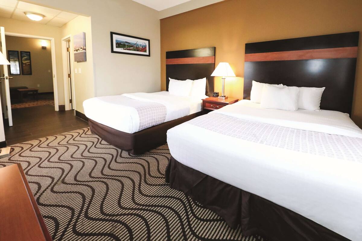 Una habitación de hotel con dos camas, una alfombra estampada y una mesita de noche con una lámpara.