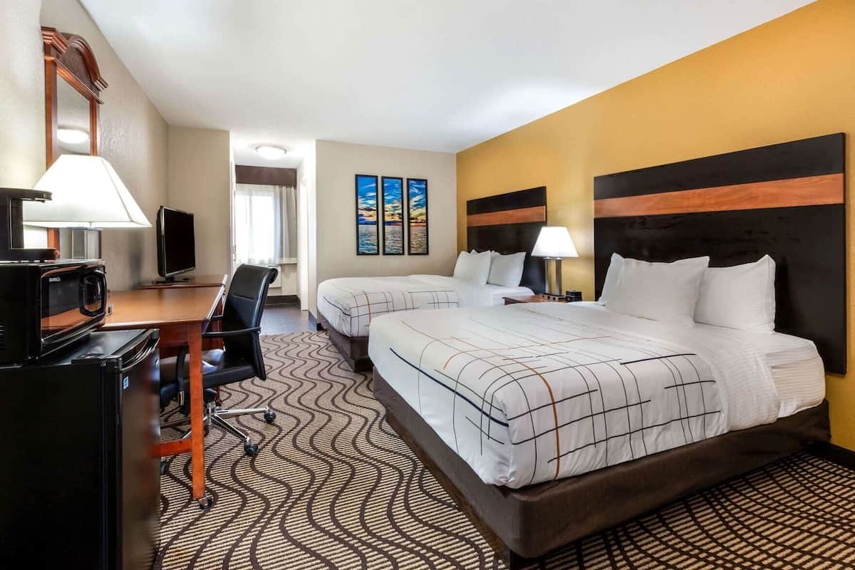 A hotel room with two beds, a desk with a TV, a chair, and artwork on the wall.