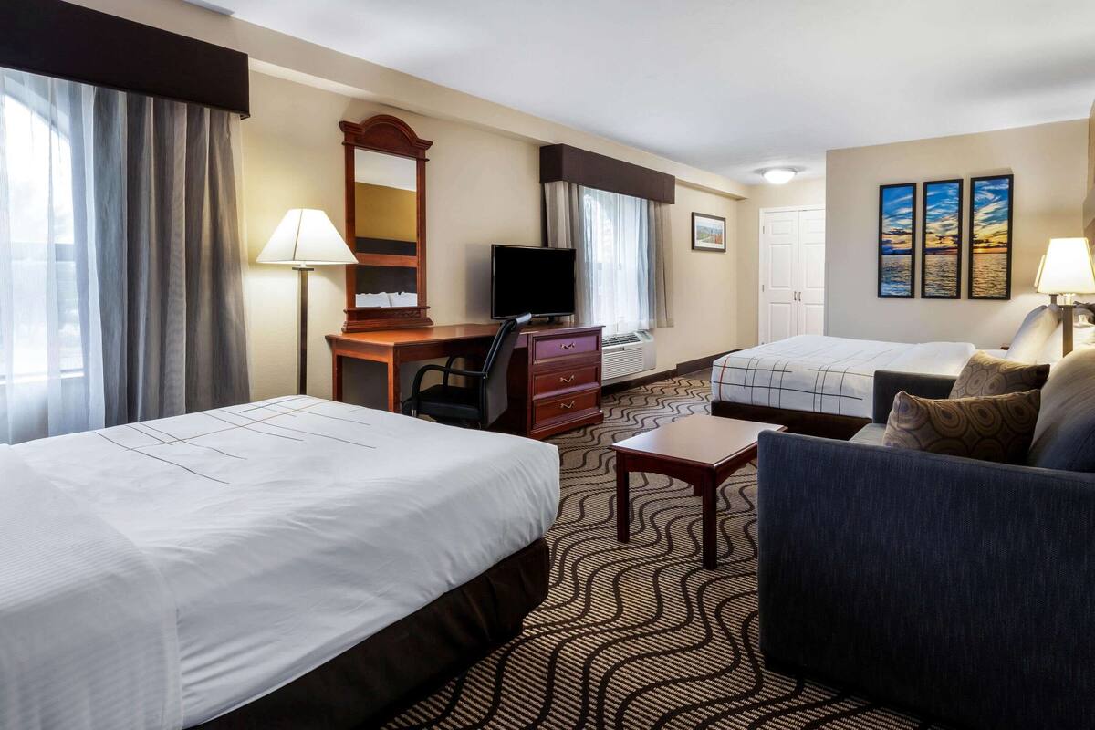 Habitación de hotel con dos camas, un escritorio con computadora, televisor, una silla y un sofá.