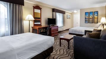 Ein Hotelzimmer mit zwei Betten, einem Schreibtisch mit Computer, einem Fernseher, einem Sessel und einem Sofa.