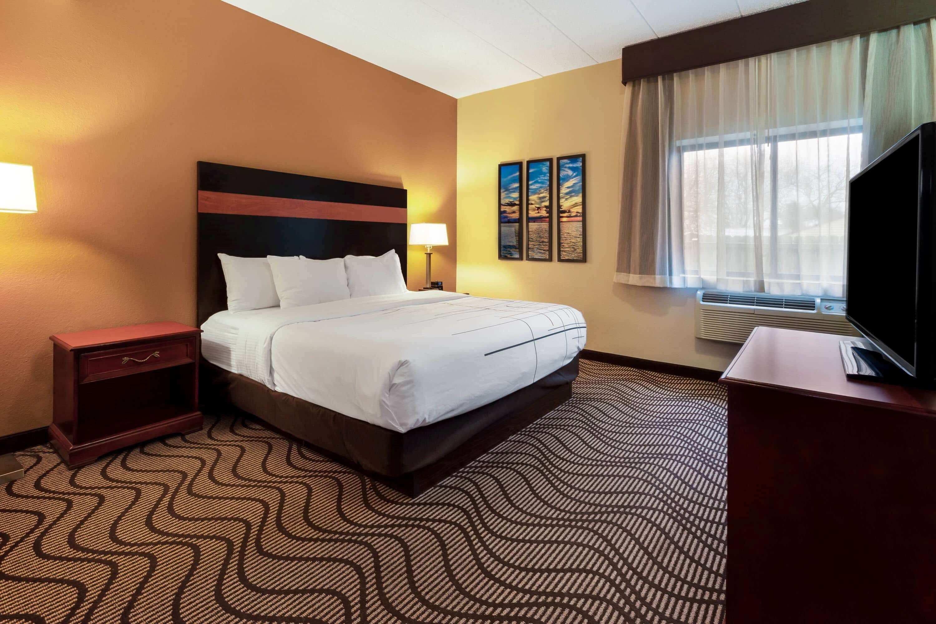 A hotel room with a bed, a nightstand, a TV, and a window with curtains.