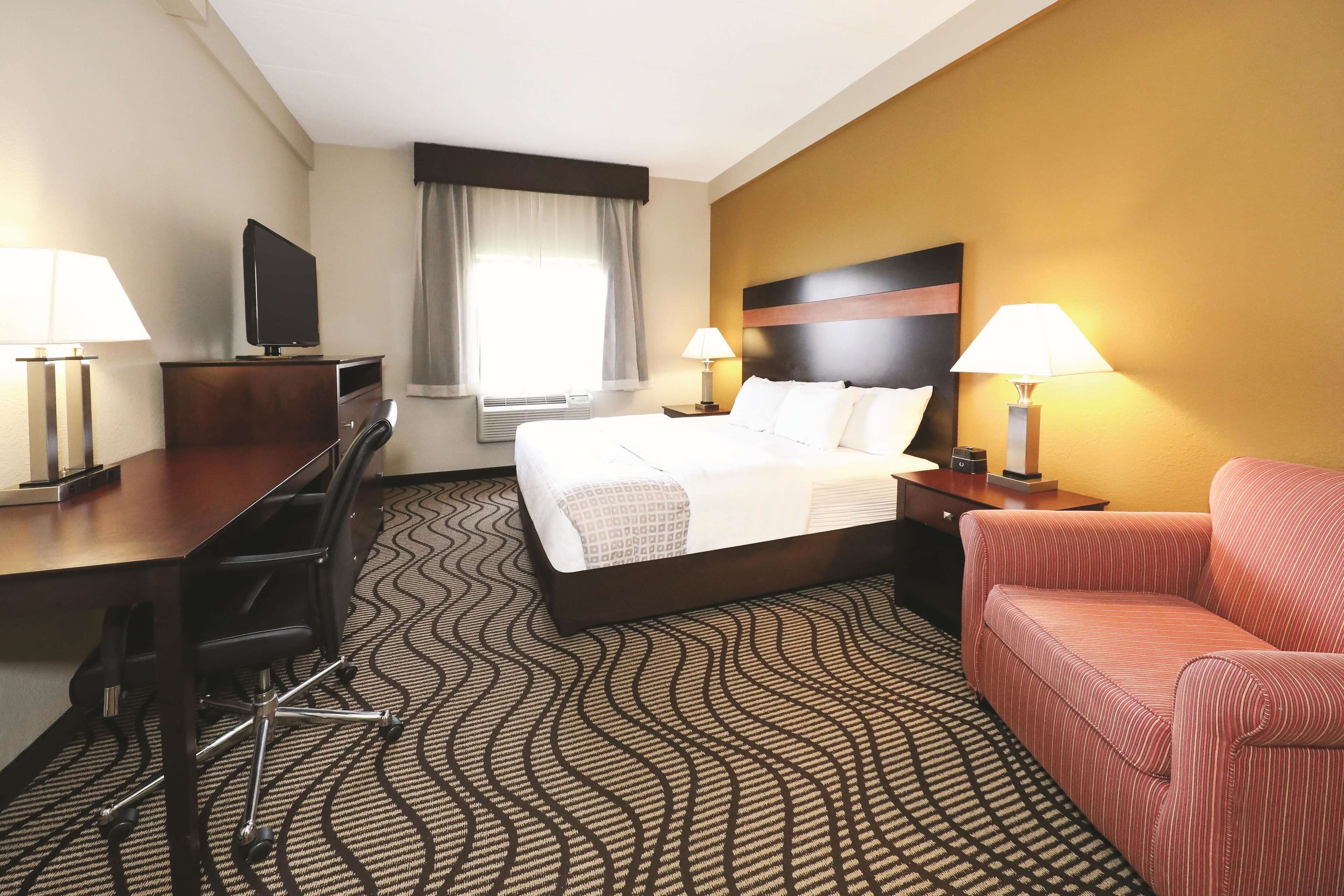A hotel room with a bed, a desk, a chair, a sofa, and two lamps.