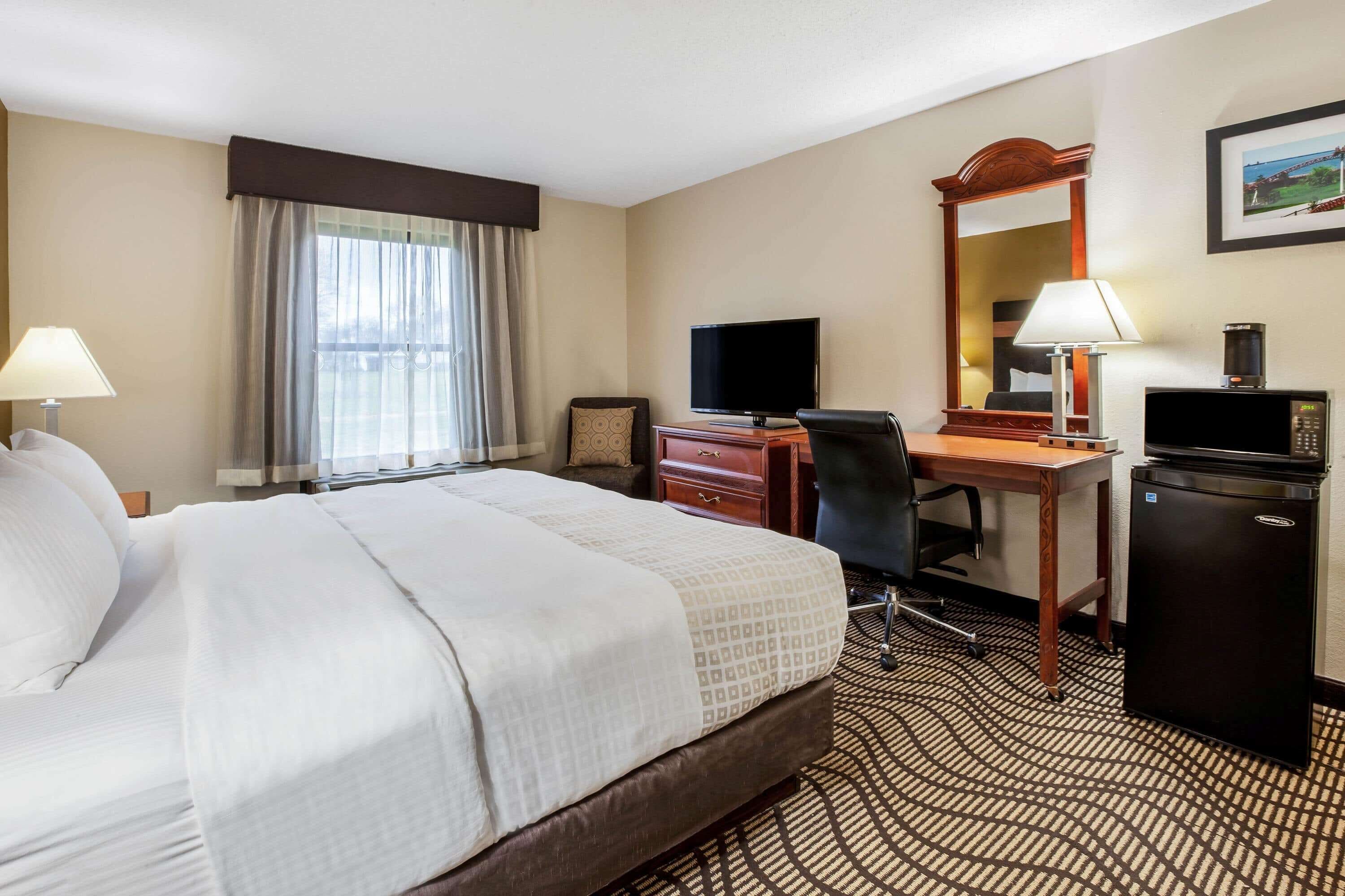 A hotel room with a large bed, a desk with a computer, a television, a coffee maker, and a small refrigerator.