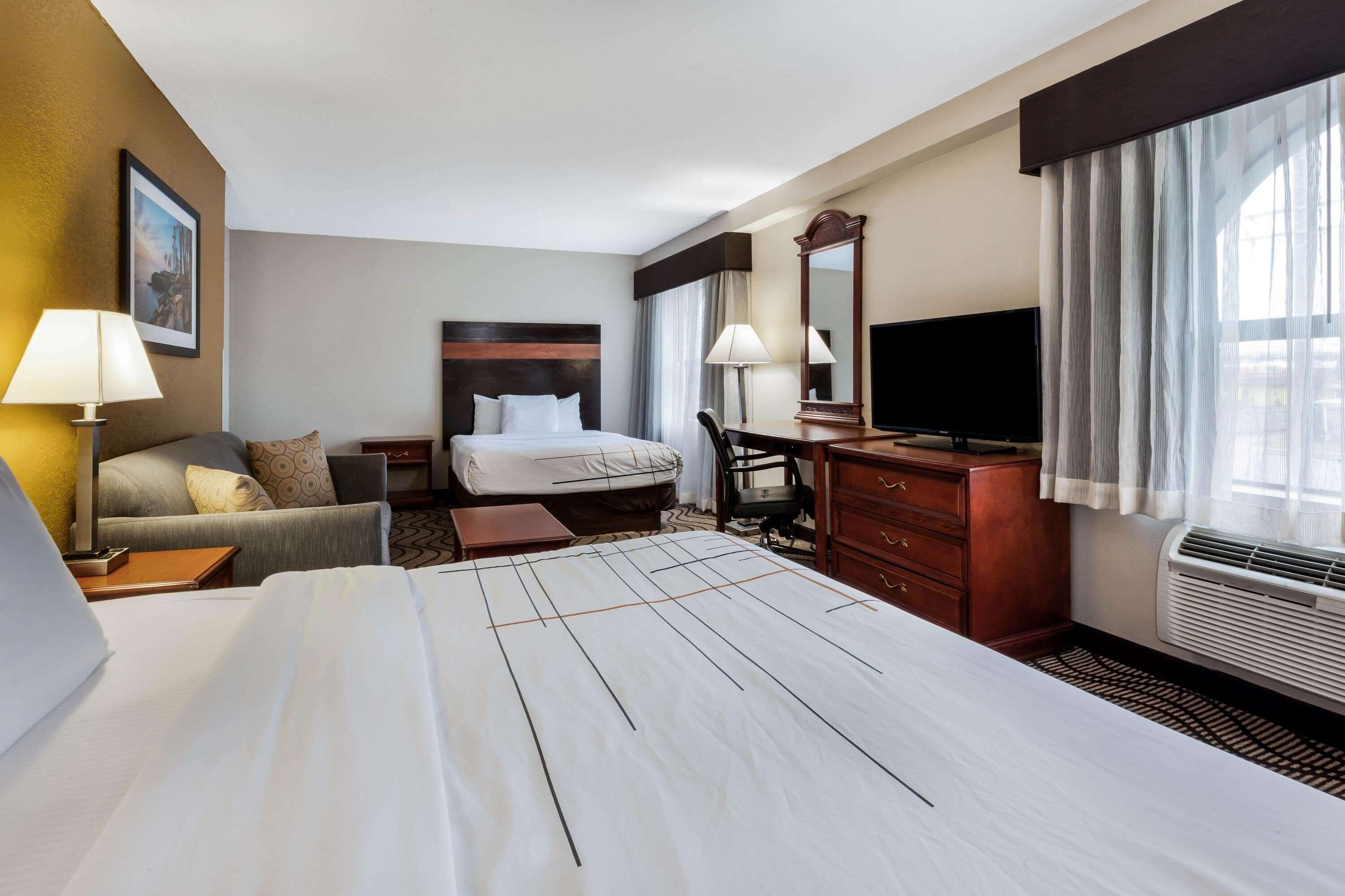 A hotel room with a large bed, a desk, a chair, a television, and a window with curtains.