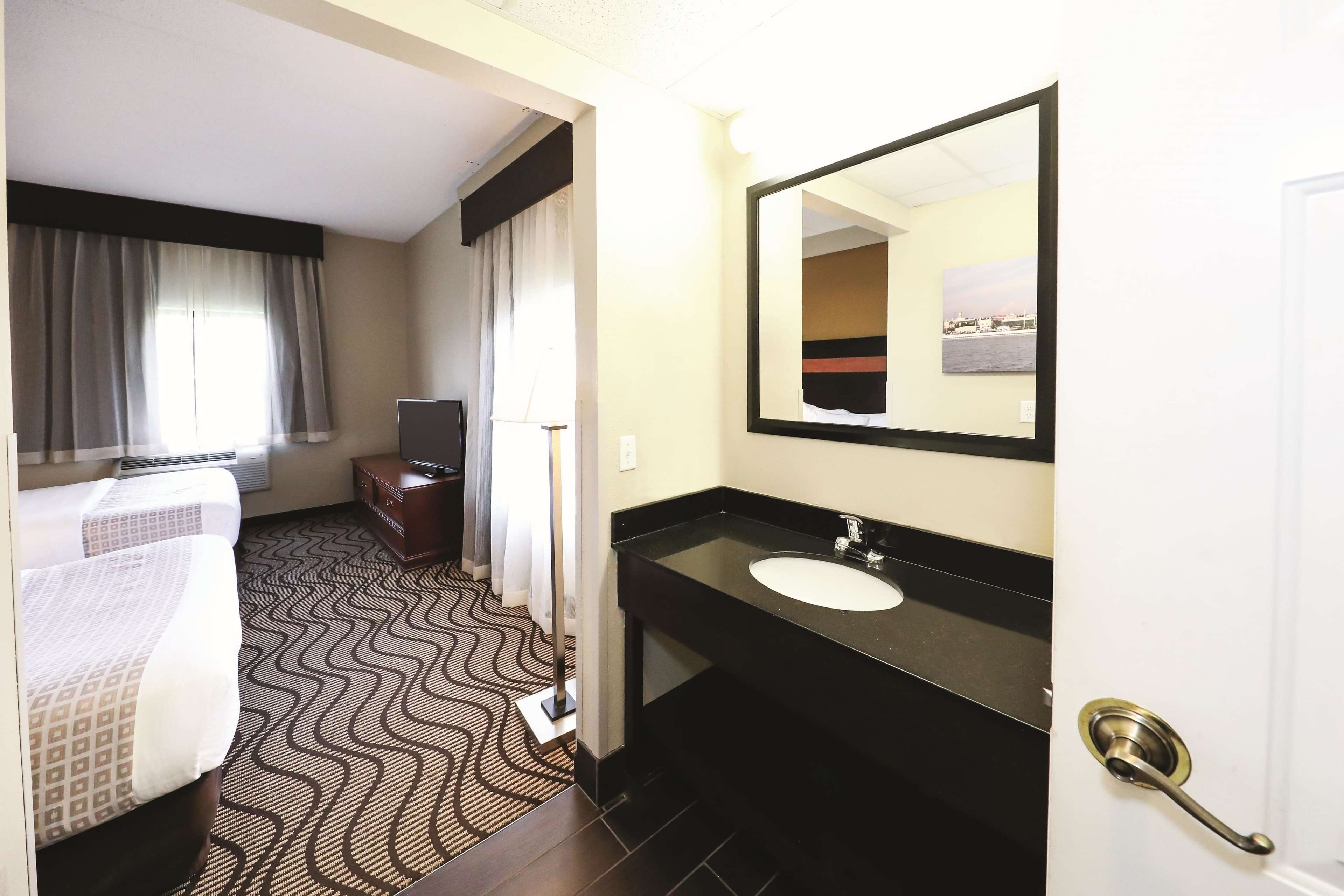 Habitación de hotel con dos camas, baño con lavamanos y espejo, y una televisión.