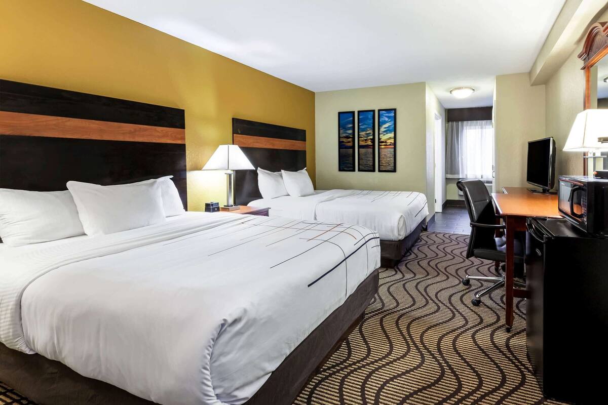 Una habitación de hotel con dos camas, un escritorio con computadora, televisión y microondas.