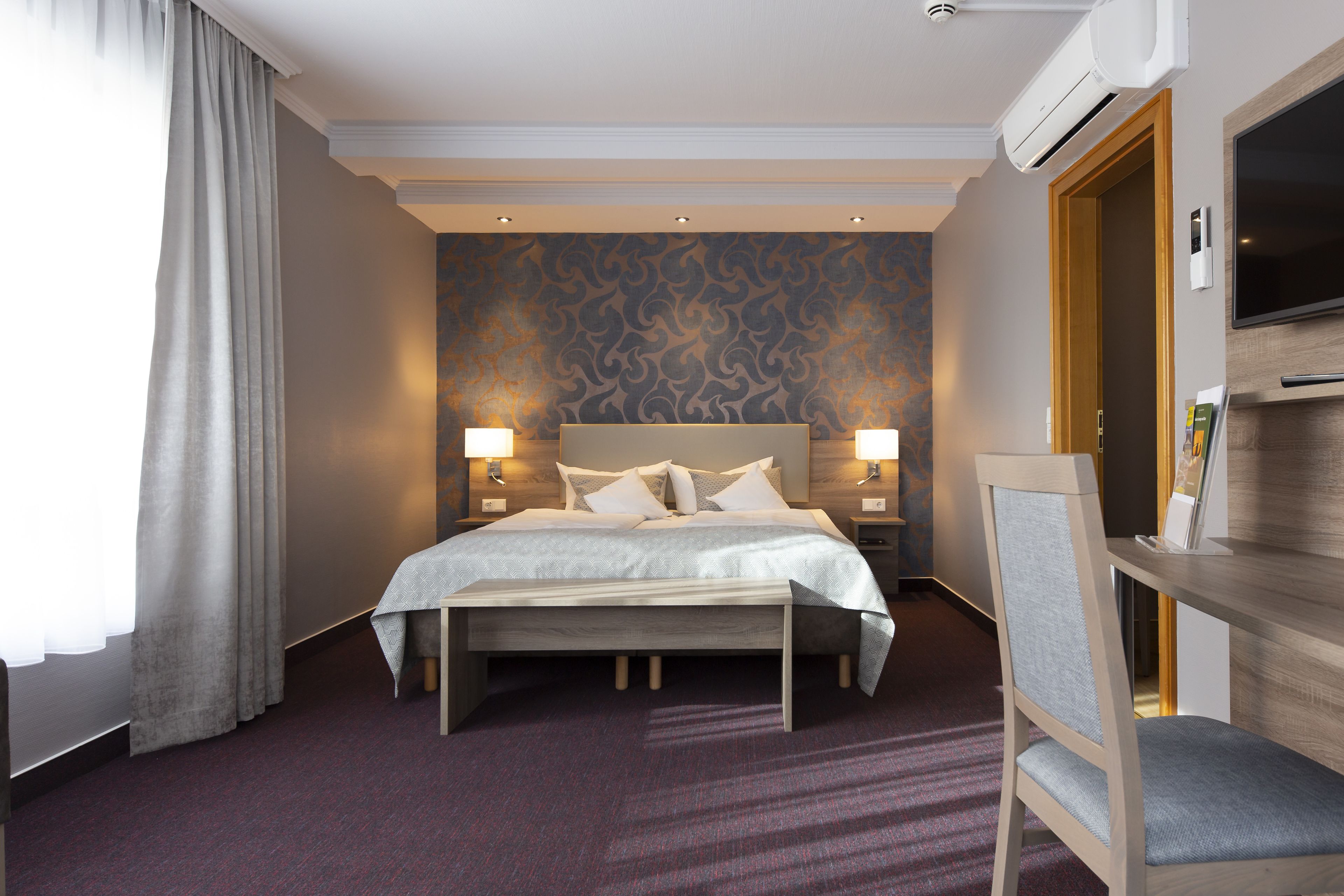 Ein Hotelzimmer mit einem großen Bett, Nachttischlampen, einem Fernseher und einem Schreibtisch mit Stuhl.