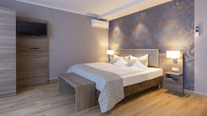 A modern bedroom with a large bed, bedside lamps, a bench, a TV, and an air conditioning unit. - Mercure Hotel Mainz City Center (Mainz)
