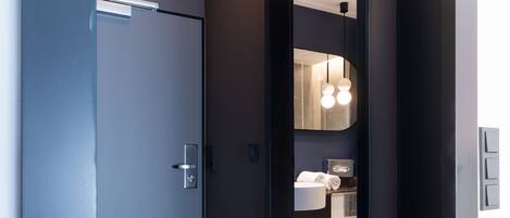 Un pasillo moderno con suelo de mármol, una puerta que da a un baño y una lámpara en el techo.