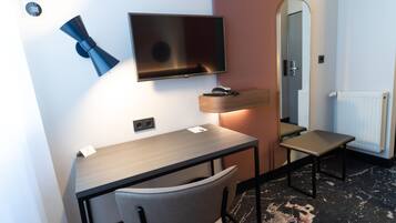 A modern hotel room with a desk, chair, flat-screen TV, bedside table, and a mirror.