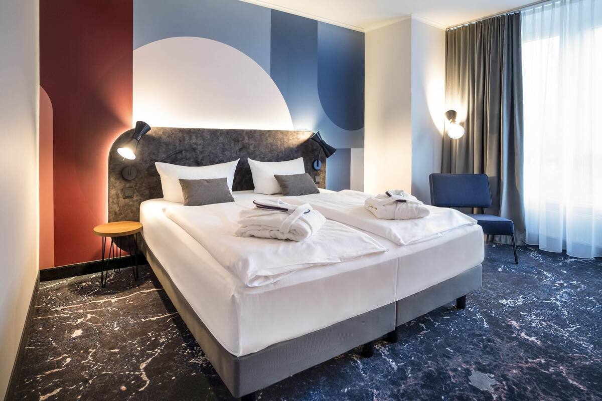 A hotel room with a large bed, a bedside table, a chair, and a view of the outdoors.