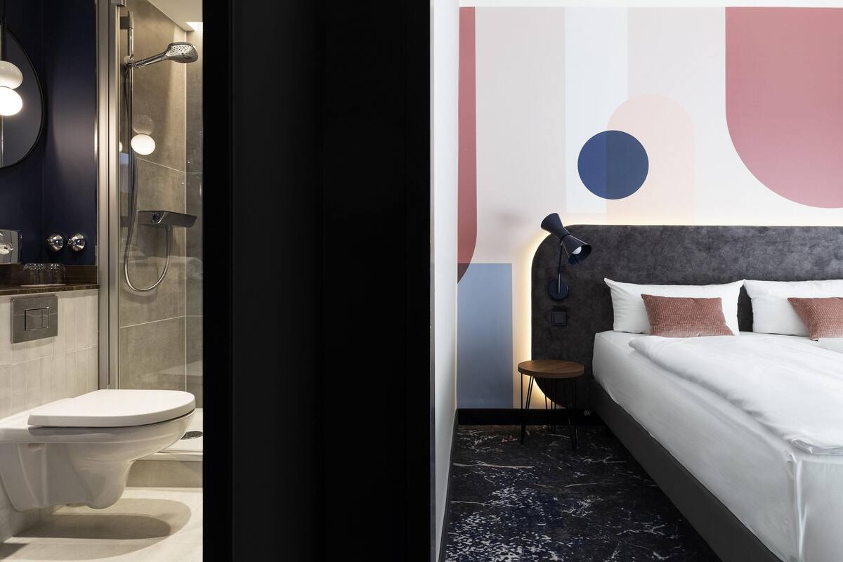 A modern bathroom with a shower, toilet, and a bed with a headboard and pillows.