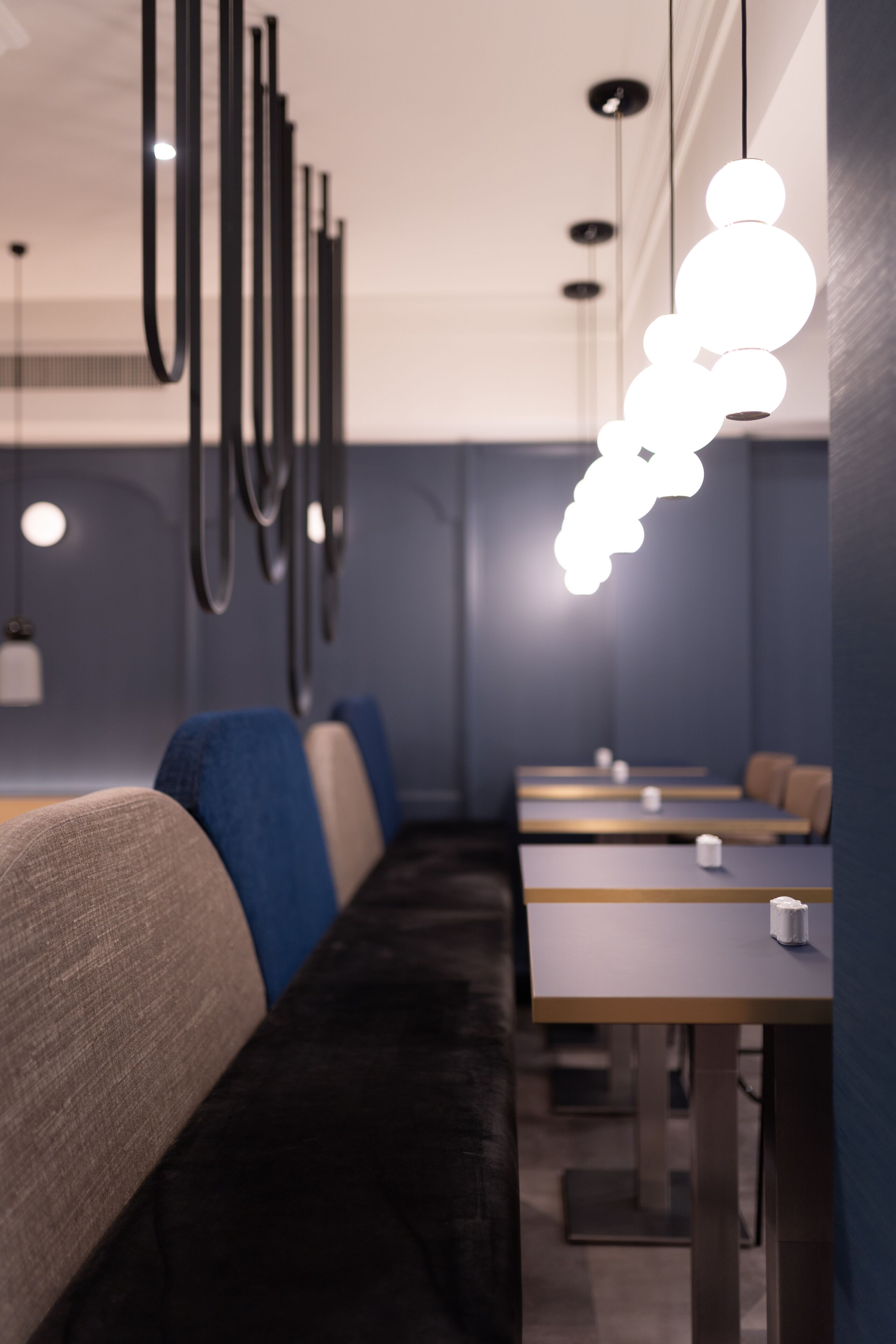 Interior moderno de restaurante con un largo banco, mesas e iluminación colgante.