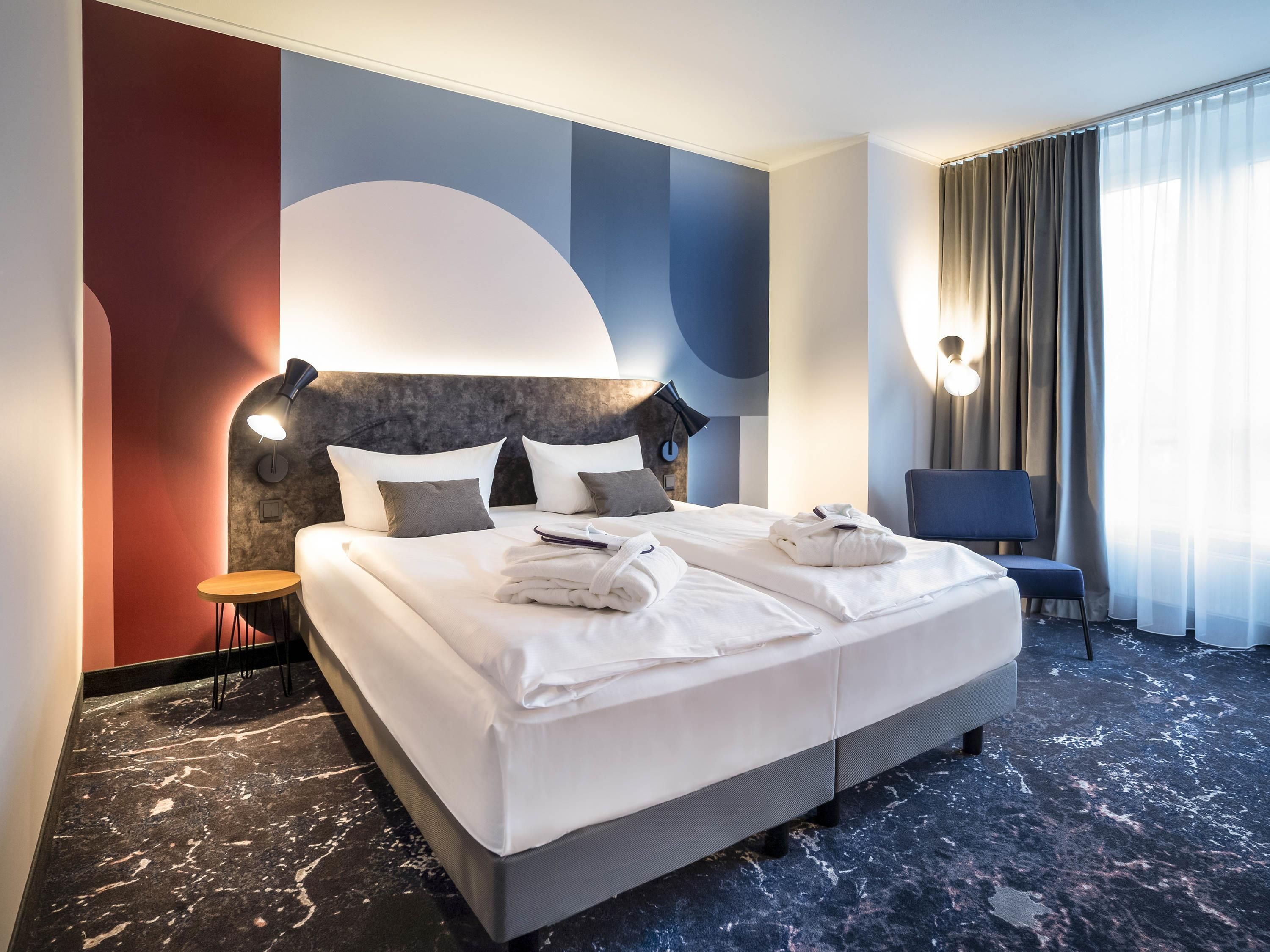 Habitación de hotel con una cama grande, una mesita de noche, una silla y vistas al exterior.