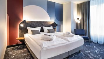 Habitación de hotel con una cama grande, una mesita de noche, una silla y vistas al exterior.