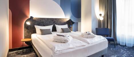 A hotel room with a large bed, a bedside table, a chair, and a view of the outdoors.