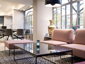 A modern lounge area with a sofa, a glass-top table, and a large vase. - Mercure Hotel Mainz City Center (Mainz)