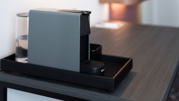 A modern coffee machine on a tray, a wall-mounted lamp, and a flat-screen TV on a wooden shelf. - Mercure Hotel Mainz City Center (Mainz)