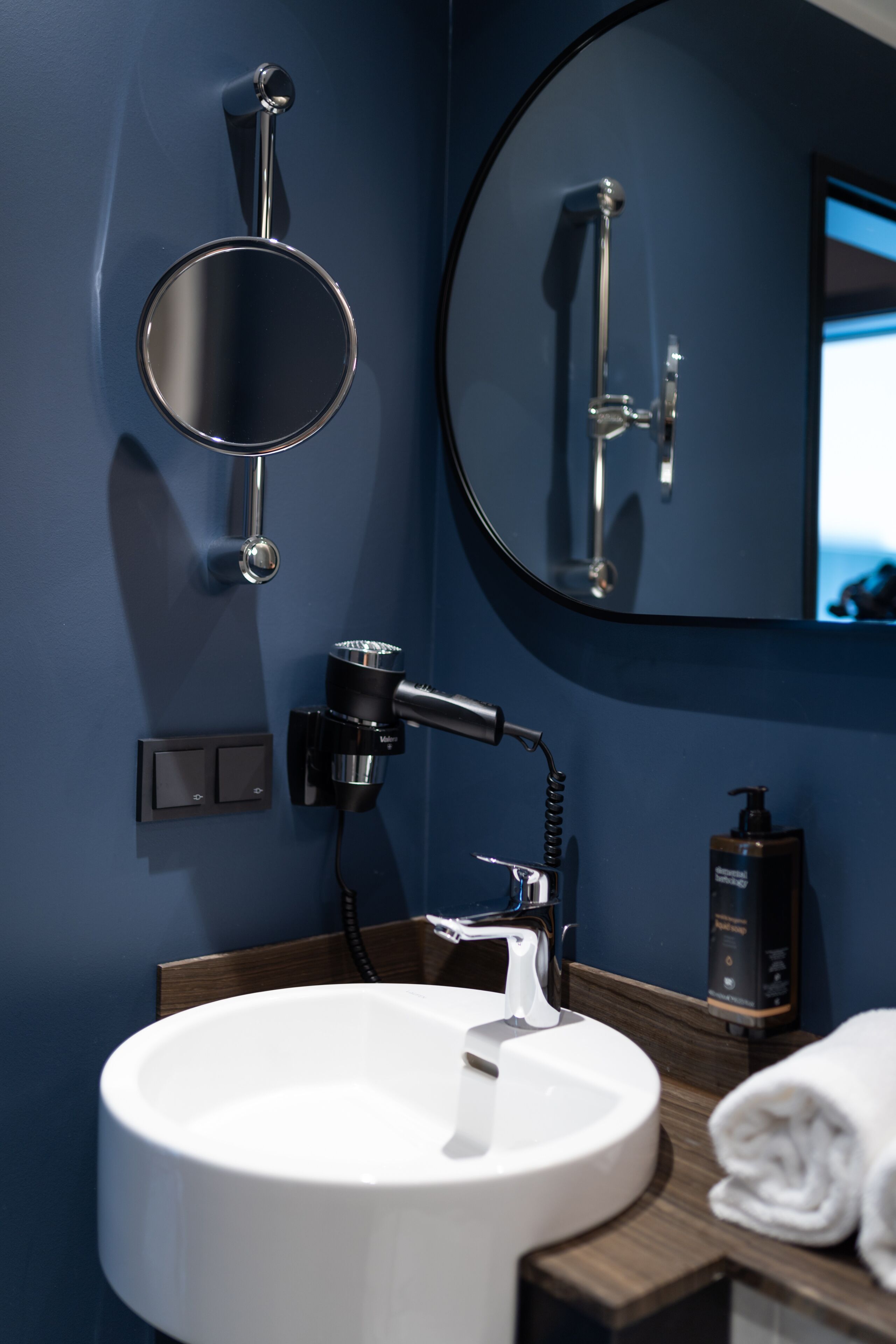 A modern bathroom with a round mirror, a white sink, and a handheld showerhead.