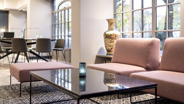 A modern lounge area with a sofa, a glass-top table, and a large vase. - Mercure Hotel Mainz City Center (Mainz)