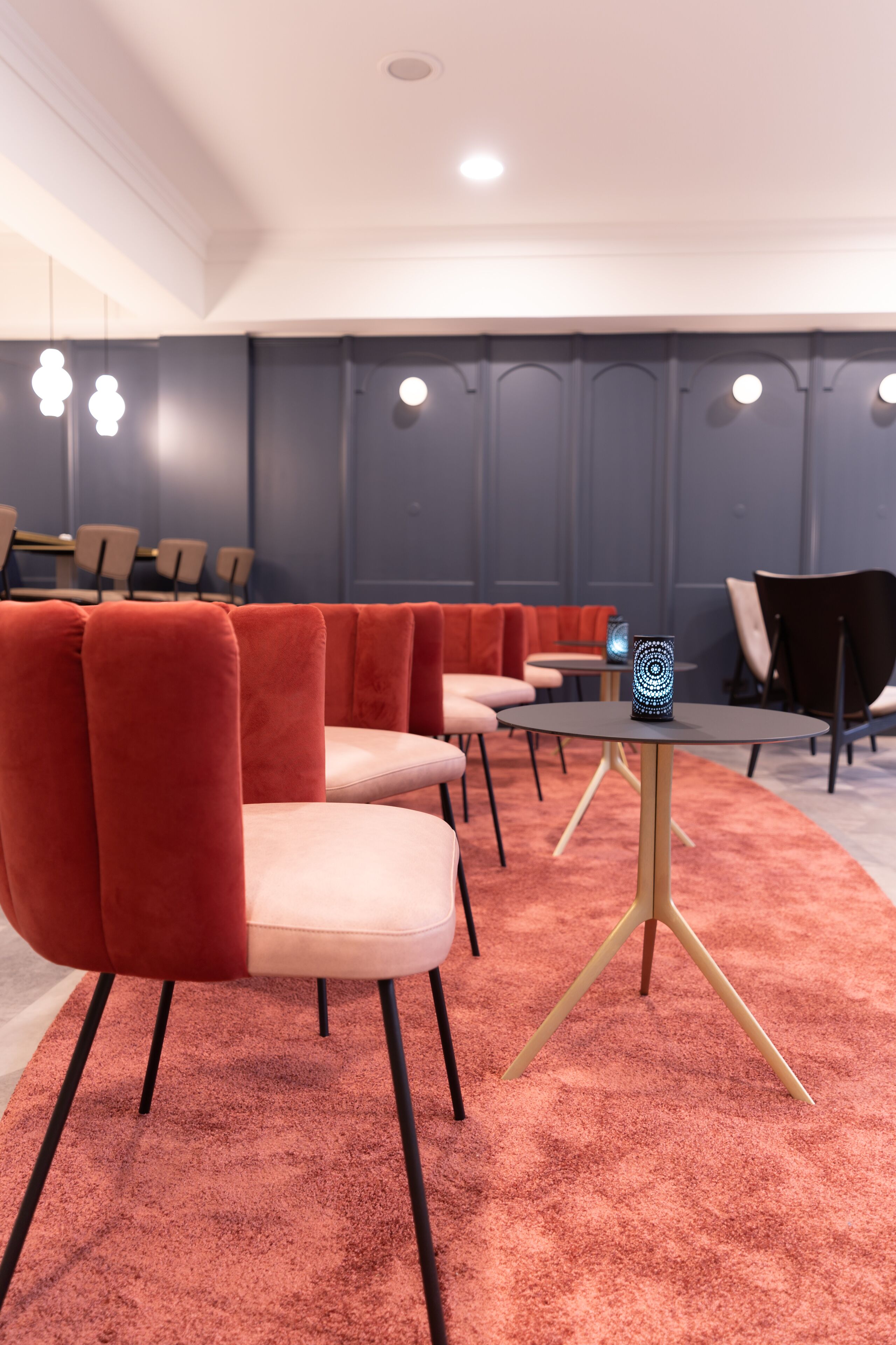 A modern conference room with red upholstered chairs, a round table with a unique blue light, and a carpeted floor.