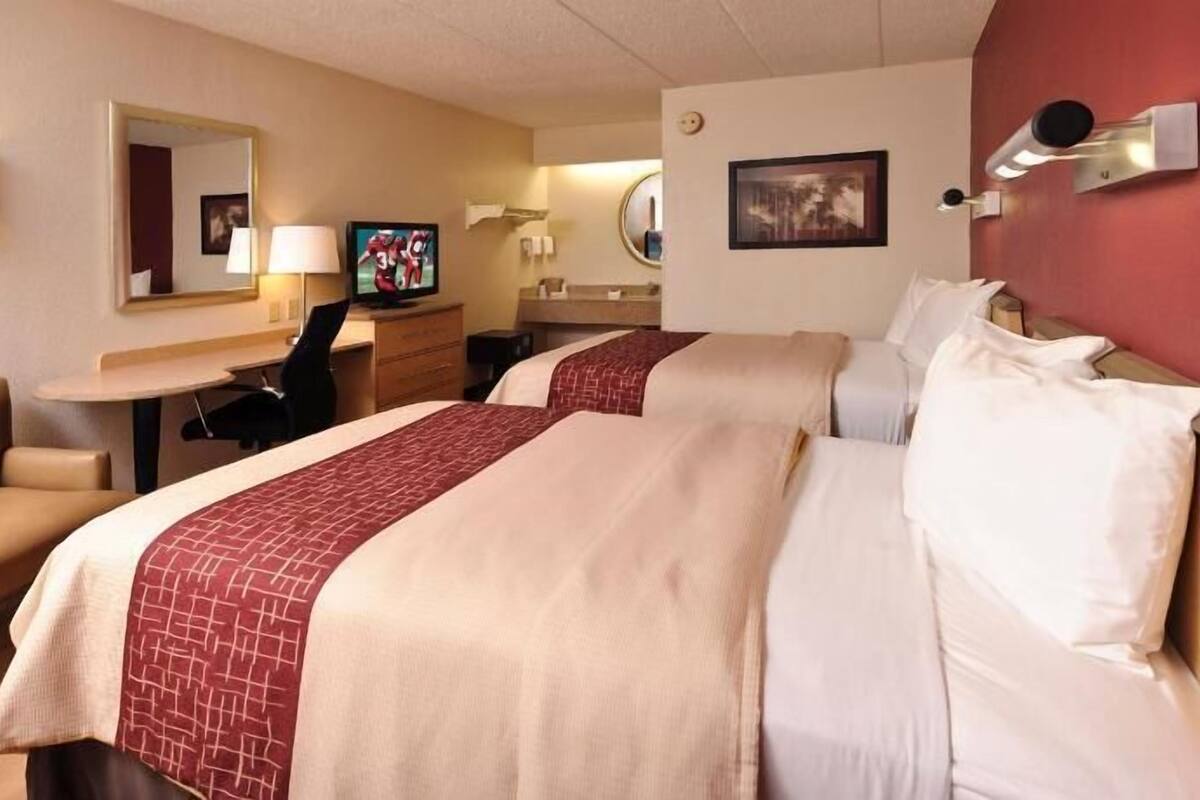 A hotel room with two beds, a desk, a chair, a TV, and a mirror.