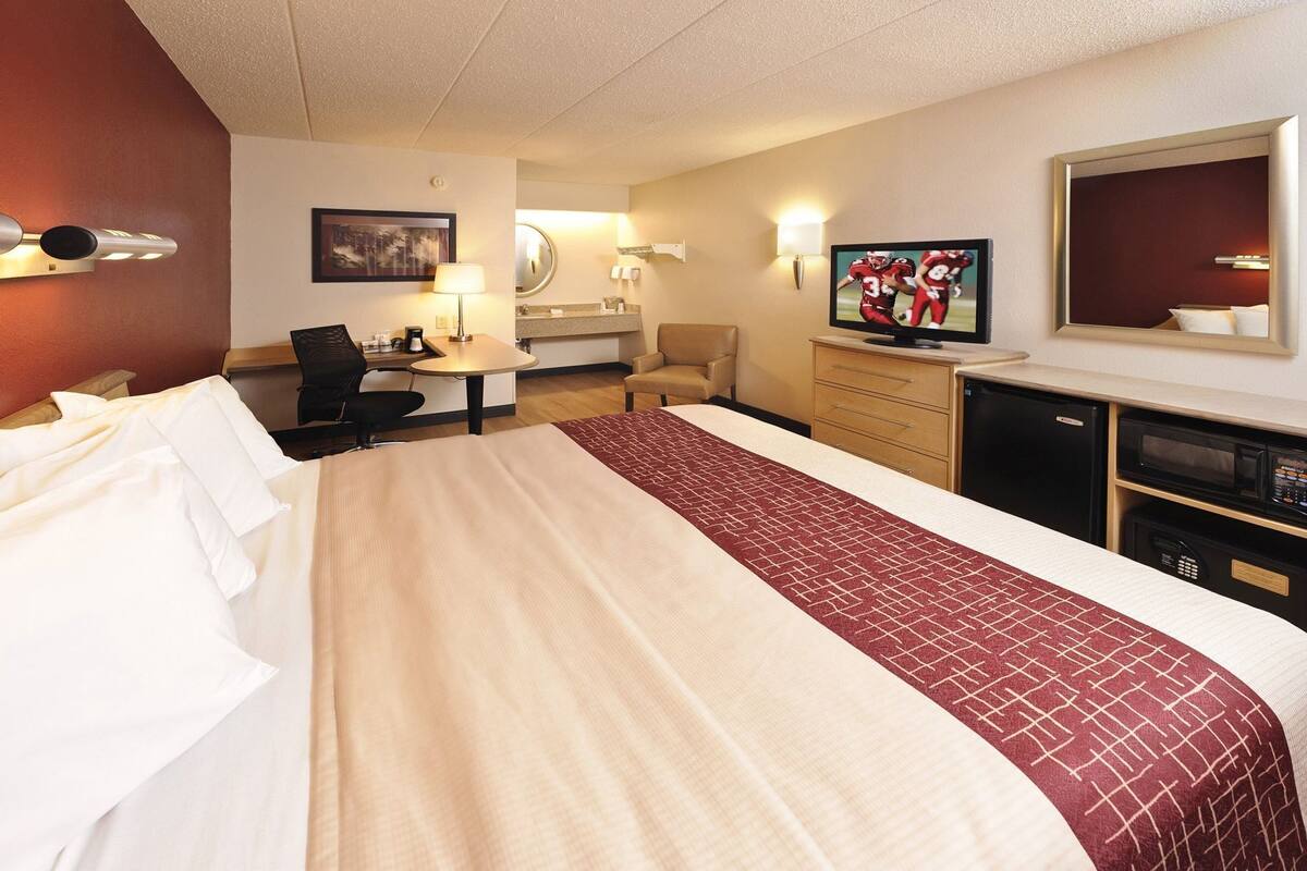 A hotel room with a large bed, a desk, a chair, a television, and a microwave.