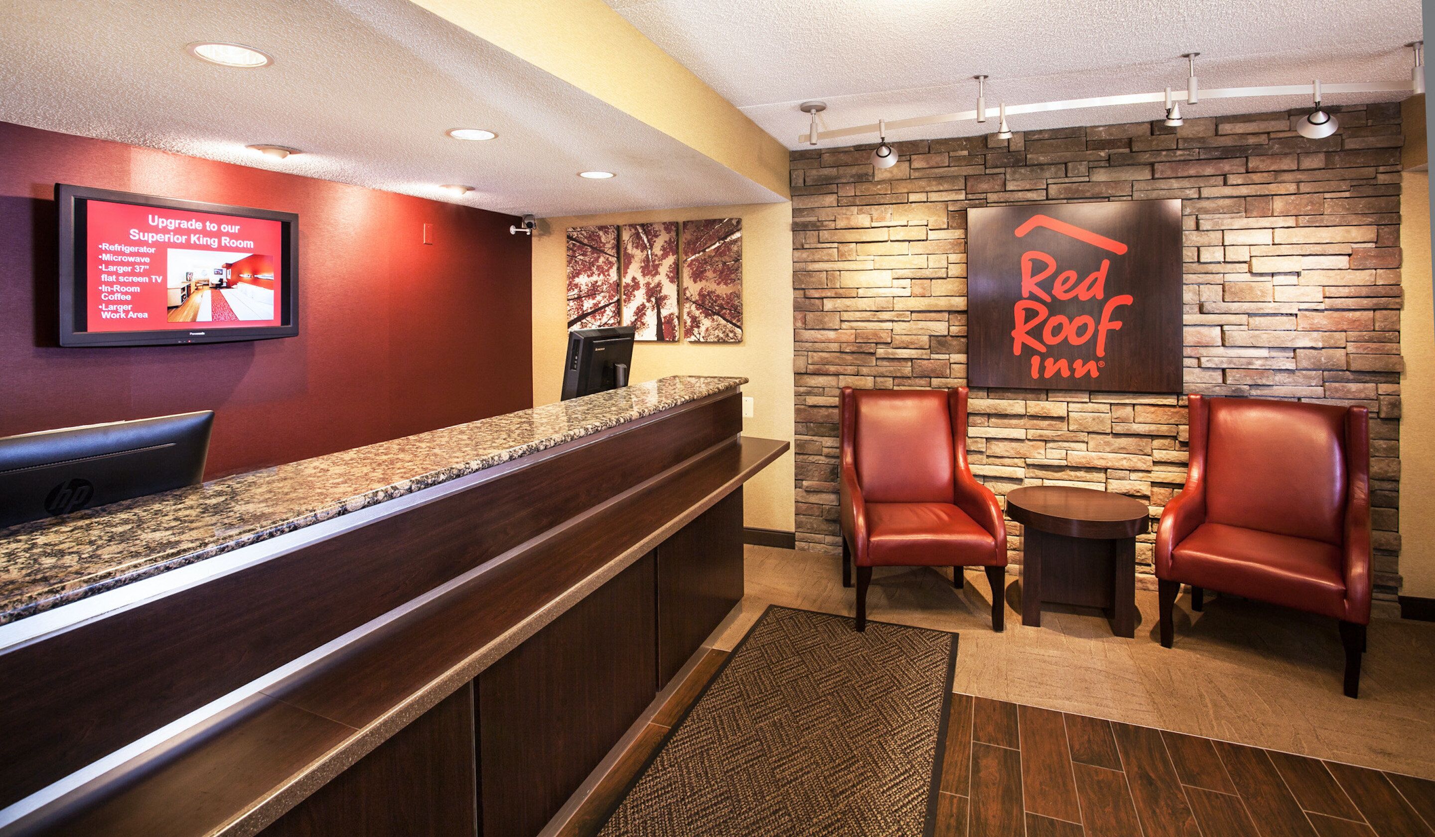 A Red Roof Inn reception area with a granite counter, leather chairs, and a stone wall backdrop.