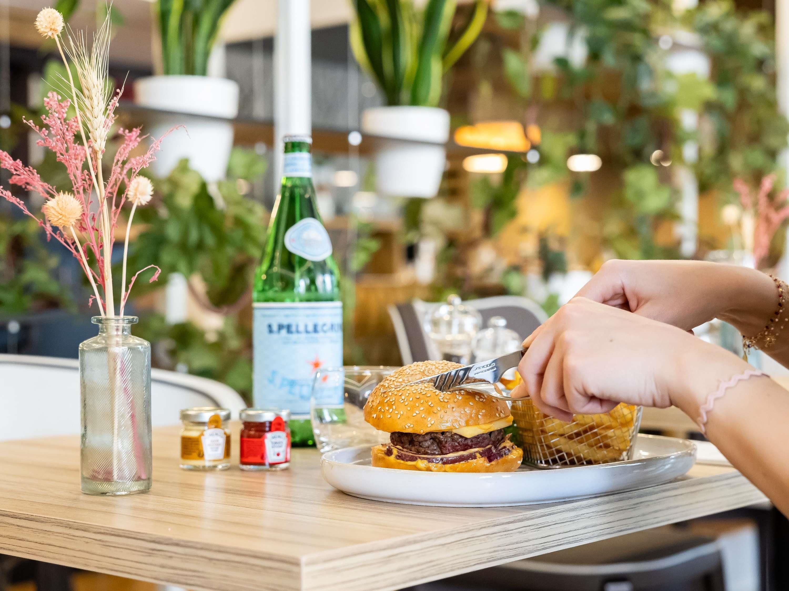 A dining table with a plate of food, a bottle of beverage, and a vase with dried flowers.