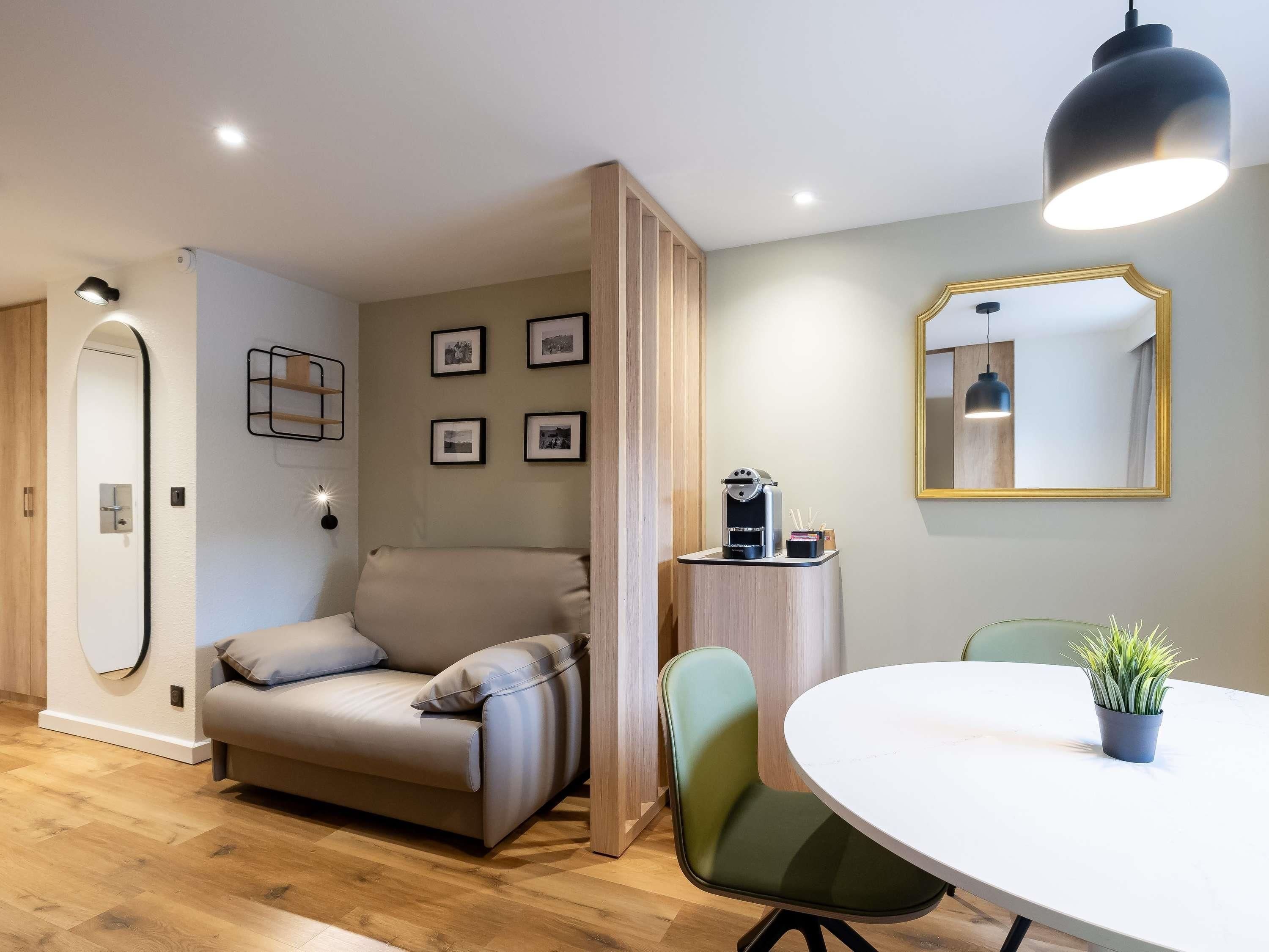 A modern living room with a sofa, a dining table, a coffee machine, and a mirror.