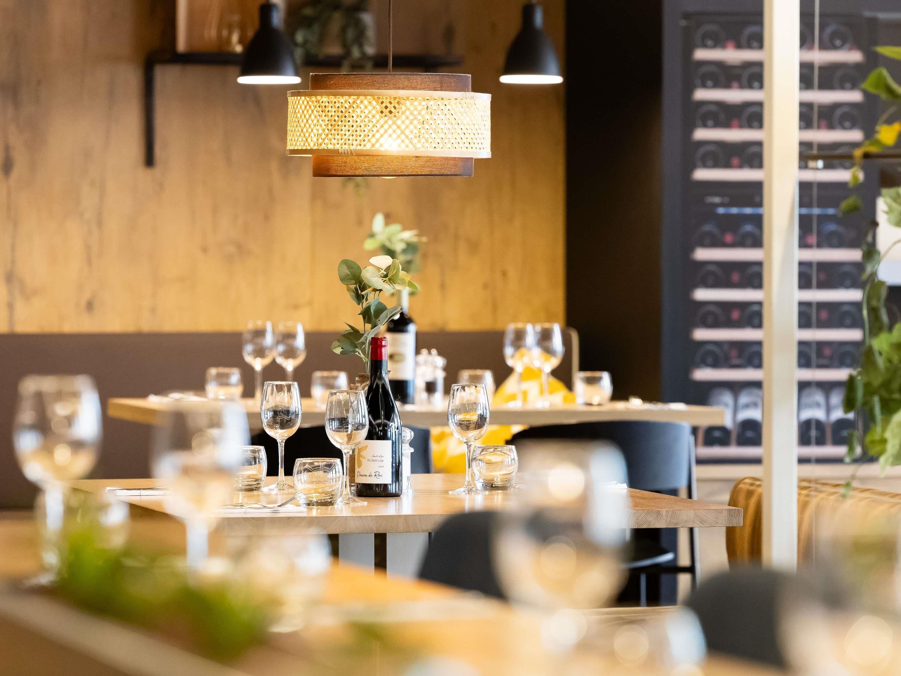 A restaurant setting with tables set for dining, a wine bottle, and a decorative plant.