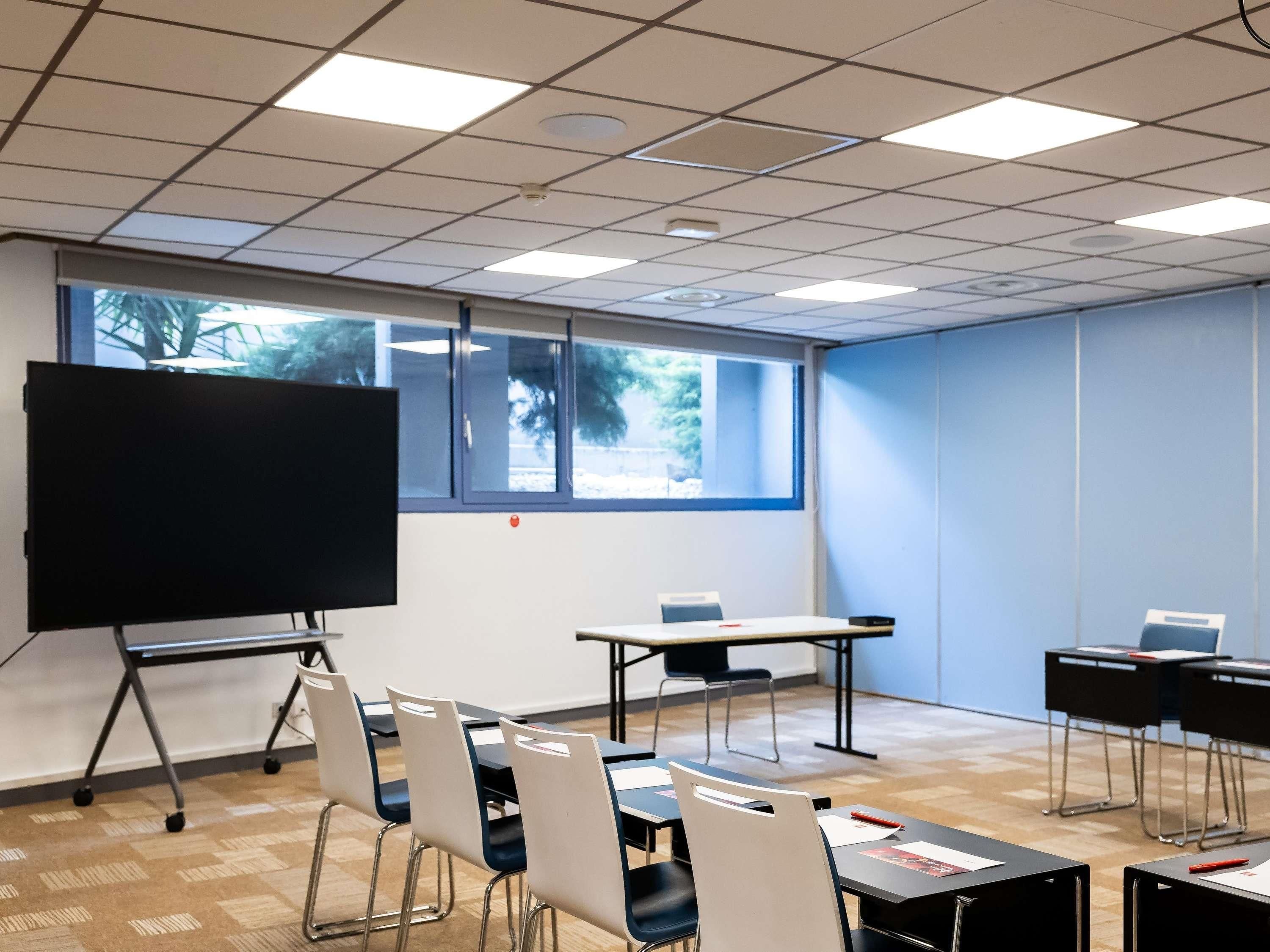A conference room with a large blackboard, tables, chairs, and a view through the window.