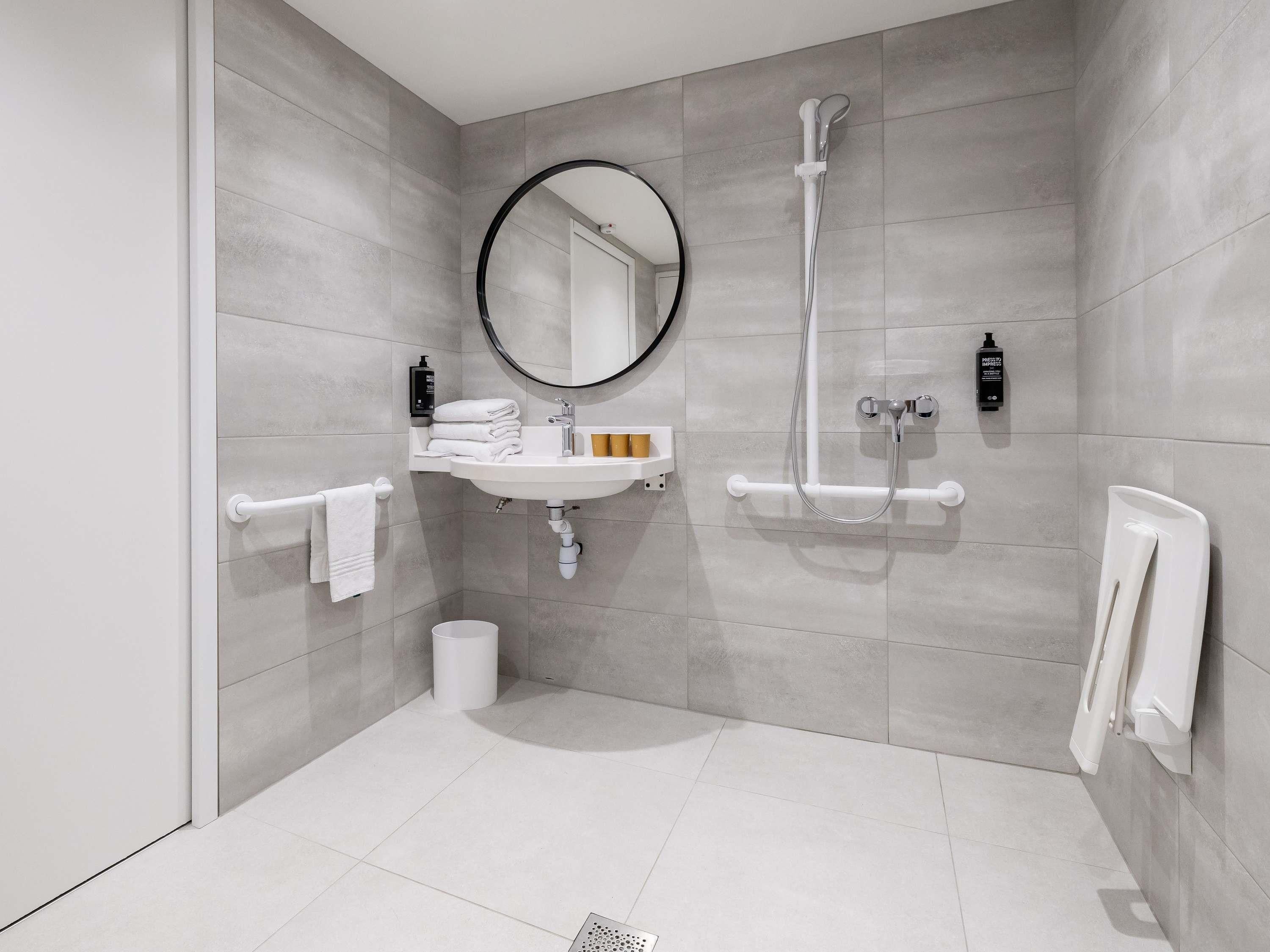 Un baño moderno con lavamanos, espejo, toallero y ducha.
