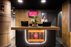 A reception desk with a digital screen displaying a menu, a potted plant, and two laptops.