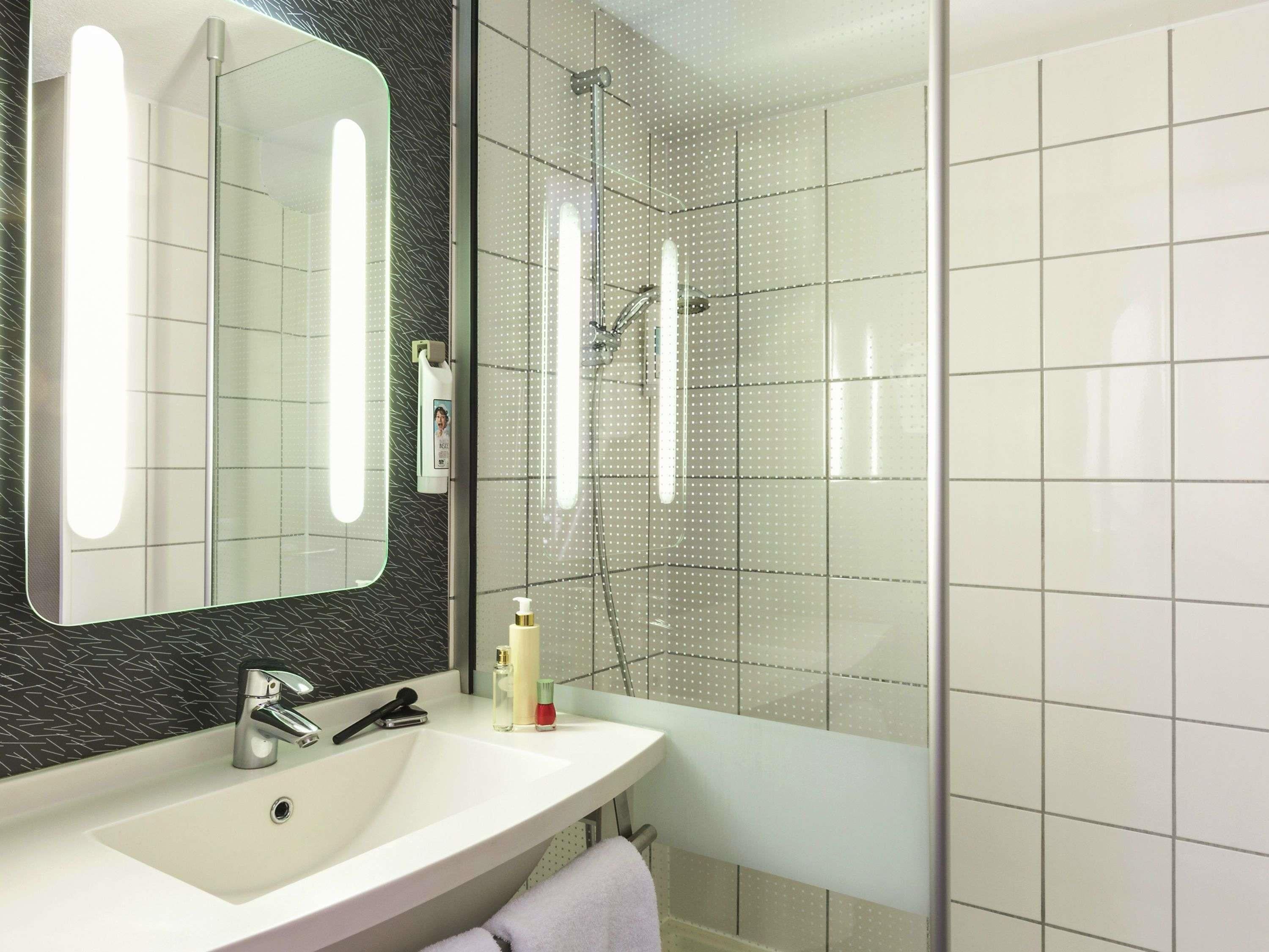 Un baño con lavamanos blanco, un espejo, un cabezal de ducha de mano y una ducha con mampara de vidrio.