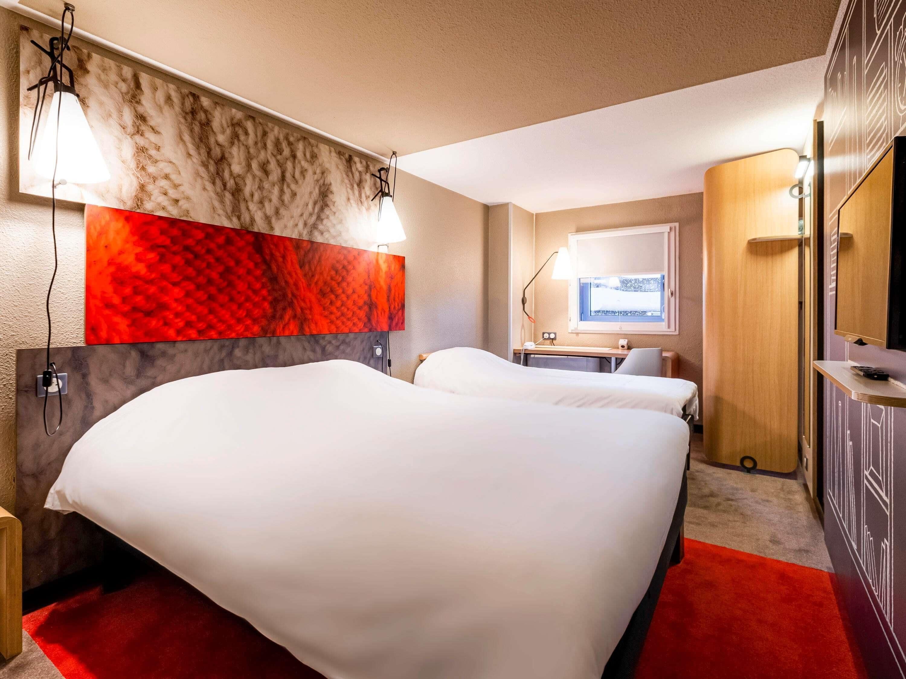 A hotel room with a bed, a desk, a chair, a TV, and a window with a view.