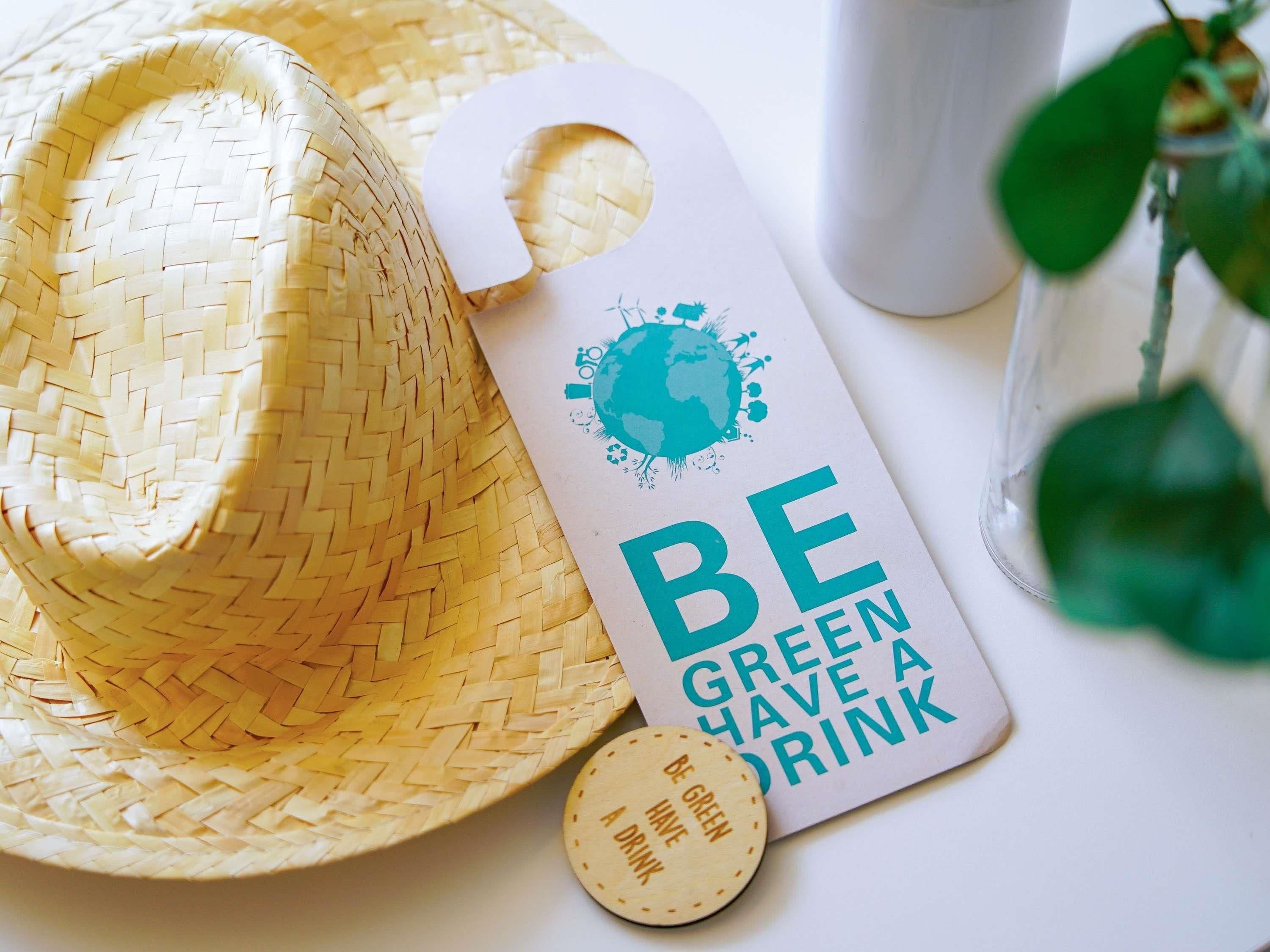 A straw hat, a bottle, and a coaster with the text 'BE GREEN HAVE A DRINK'.