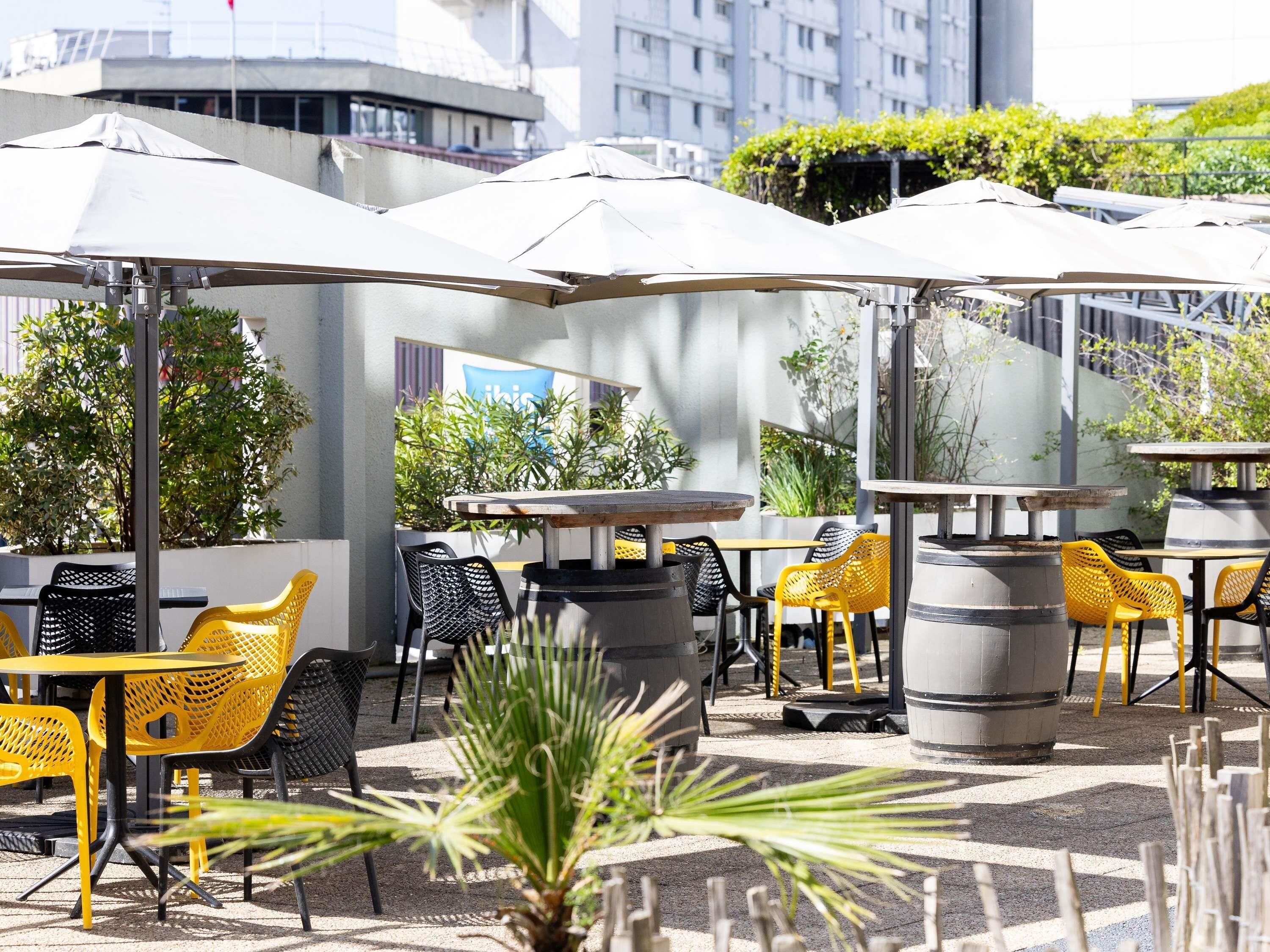 An outdoor seating area with tables and chairs, umbrellas, and potted plants.