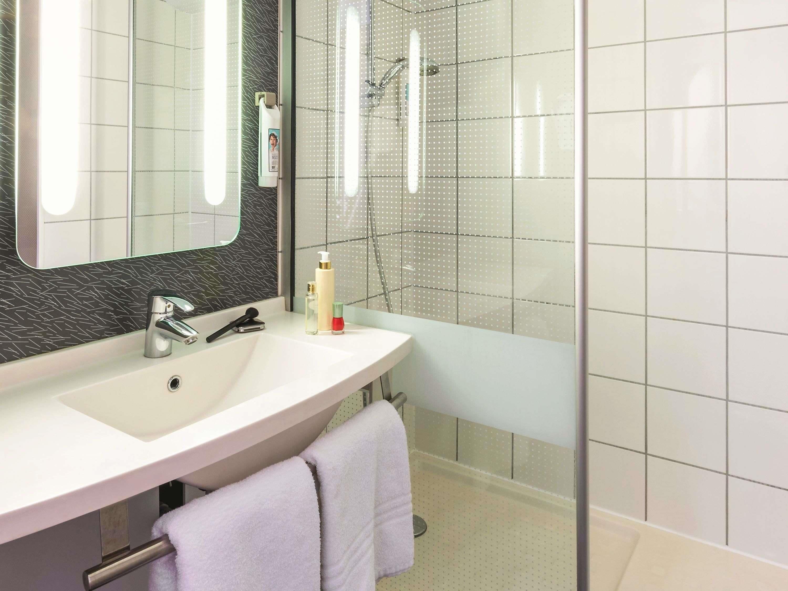 A bathroom with a white sink, a mirror, a handheld showerhead, and a glass-enclosed shower area.