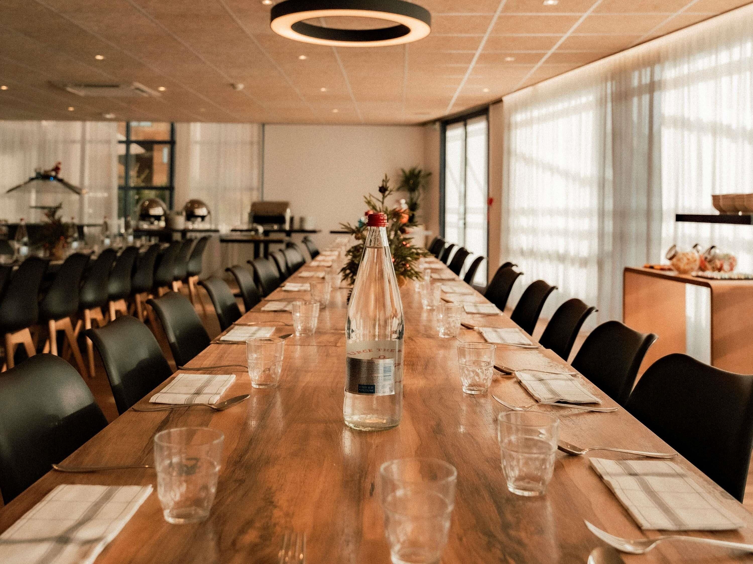 Un salón de conferencias con una larga mesa de madera, sillas, una botella de agua y una planta pequeña.