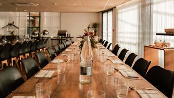 Un salón de conferencias con una larga mesa de madera, sillas, una botella de agua y una planta pequeña.