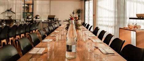 Un salón de conferencias con una larga mesa de madera, sillas, una botella de agua y una planta pequeña.