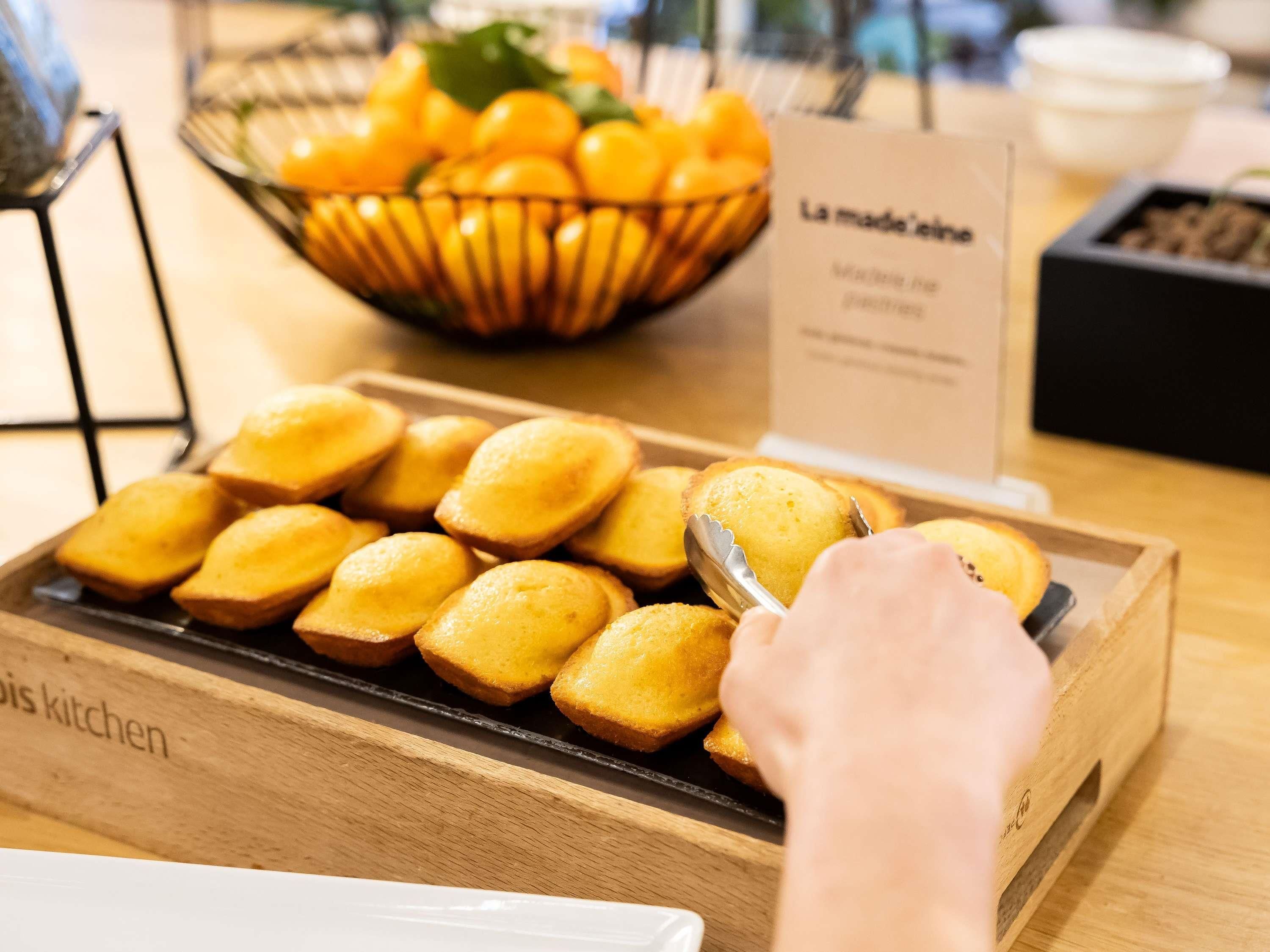 A tray of golden-brown pastries in a wooden box with a sign reading 'La madeleine'.