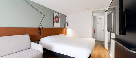 Habitación de hotel con cama, sofá, televisión, un cuadro y una puerta que da a otra habitación.