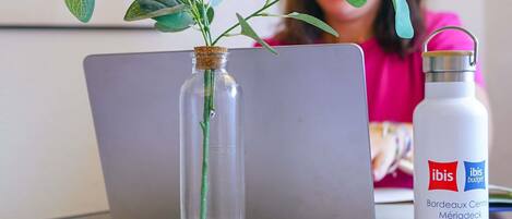 Un ordinateur portable, une bouteille en verre contenant une plante et une bouteille d’eau sur une table.